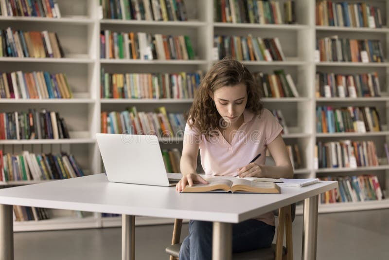 College student writing notes beside a laptop in a contemporary library setting